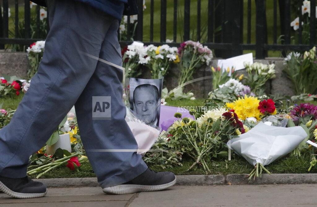 Frank Augstein A man walks past a photo of Britain's Prince Philip among flowers left by the public outside the gates of Windsor Castle, a day after the death of Britain's Prince Philip, in Windsor, England, Saturday, April 10, 2021. Britain's Prince Philip, the irascible and tough-minded husband of Queen Elizabeth II who spent more than seven decades supporting his wife in a role that mostly defined his life, died on Friday. (AP Photo/Frank Augstein)