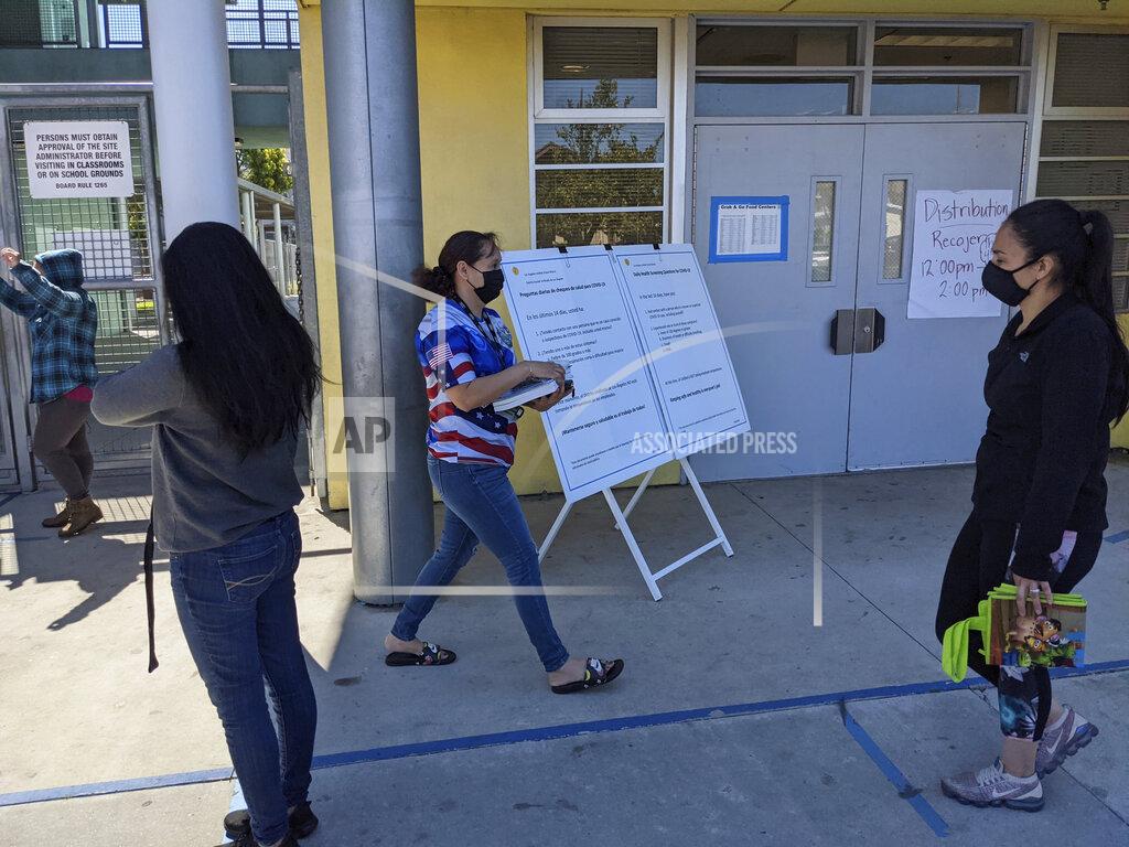Damian Dovarganes In this Tuesday, March 16, 2021, photo, parents pick up school materials outside the Aurora Elementary School in Los Angeles. Students in California classrooms can sit 3 feet apart instead of 6 under new guidelines adopted by the state as school officials figure out how to reopen campuses closed for a year during the COVID-19 pandemic. (AP Photo/Damian Dovarganes)