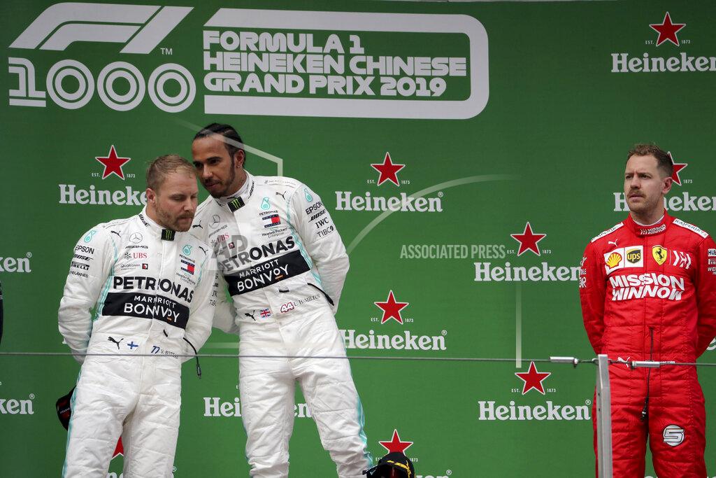 Ng Han Guan Mercedes driver Lewis Hamilton of Britain, center whispers to teammate Valtteri Bottas of Finland as Ferrari driver Sebastian Vettel of Germany at right waits for the award ceremony for the Chinese Formula One Grand Prix at the Shanghai International Circuit in Shanghai on Sunday, April 14, 2019. (AP Photo/Ng Han Guan)