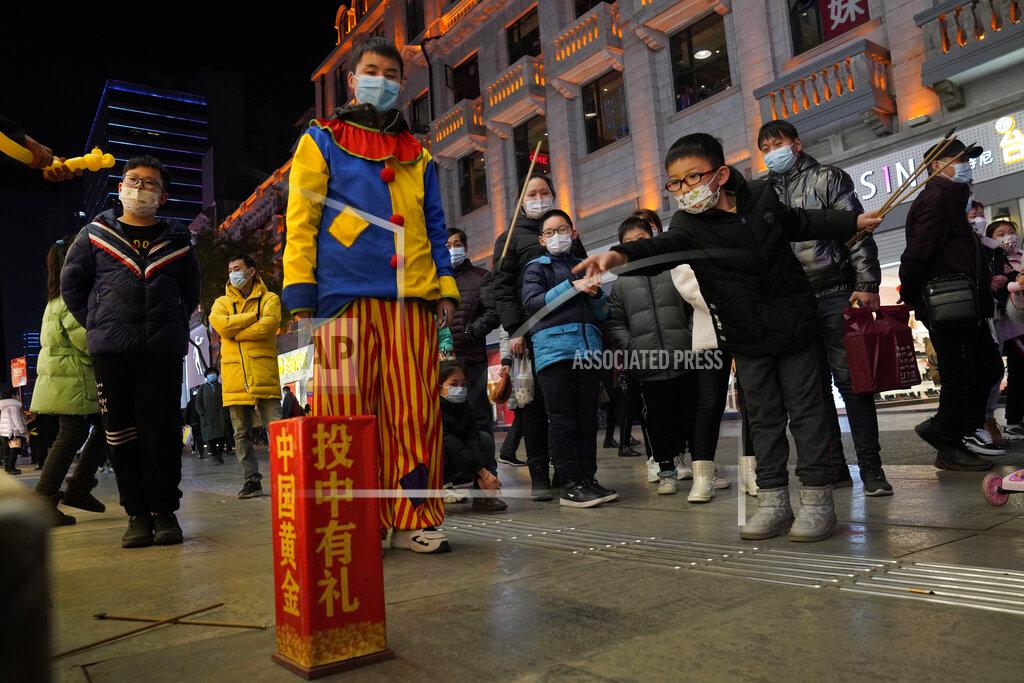 Ng Han Guan FILE - In this Jan. 15, 2021, file photo, a child attempts to throw sticks into a container to win prizes along a shopping street in Wuhan in central China's Hubei province. Couples go on dates, families dine out at restaurants, shoppers flock to stores. Face masks aside, people are going about their daily life pretty much as before in the Chinese city that was first hit by the COVID-19 pandemic. (AP Photo/Ng Han Guan, File)