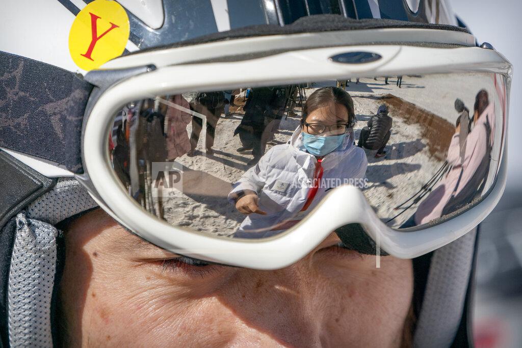 Mark Schiefelbein A staff member wearing a face mask to protect against the spread of the coronavirus is reflected in the goggles of a skier at the National Alpine Skiing Center in Yanqing on the outskirts of Beijing, Friday, Feb. 5, 2021. Beijing Olympic organizers showed off the downhill skiing venue and the world's longest bobsled and luge track Friday, one year ahead of the scheduled opening of the 2022 Olympic Winter Games. (AP Photo/Mark Schiefelbein)