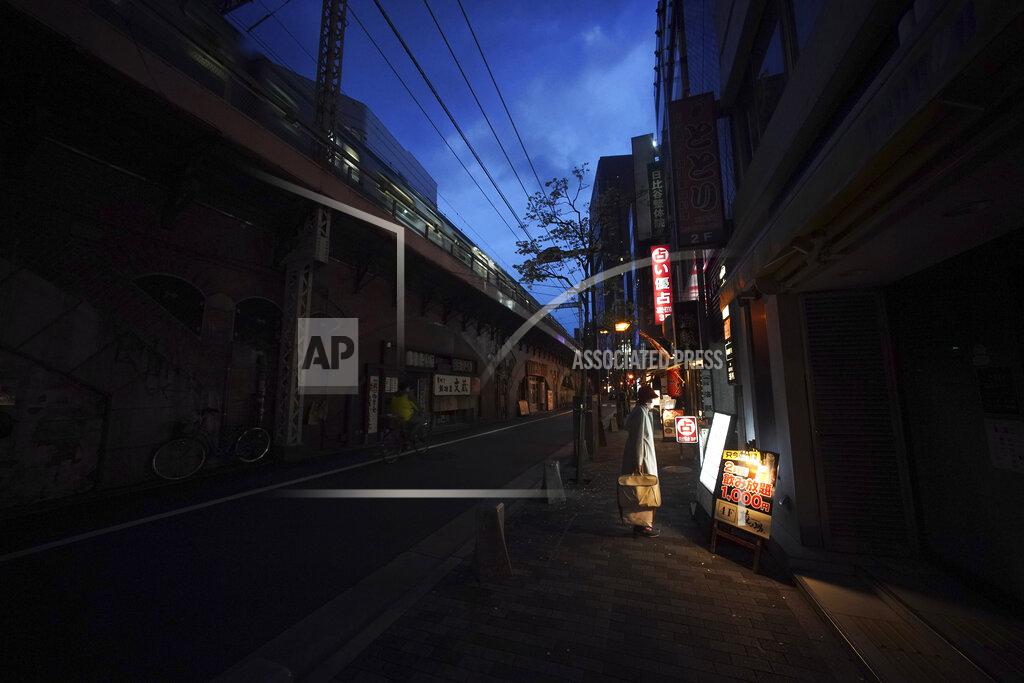 Eugene Hoshiko FILE - In this April 28, 2020, file photo, a woman wearing a face mask against the spread of the new coronavirus looks at menu of a restaurant at an empty street in Tokyo. Under Japan's coronavirus state of emergency, people have been asked to stay home. Many are not. Some still have to commute to their jobs despite risks of infection, while others are dining out, picnicking in parks and crowding into grocery stores with scant regard for social distancing. (AP Photo/Eugene Hoshiko, File)