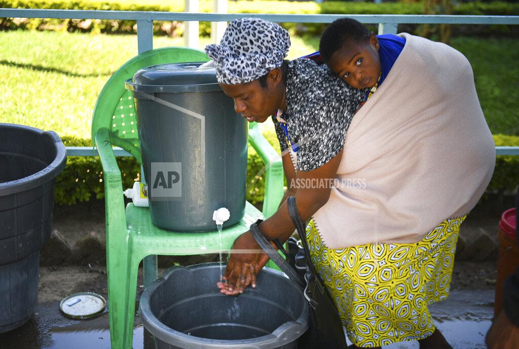 A woman carrying a child on her back washes her hands at a polling station during a presidential election in Blantyre, Malawi, Tuesday, June 23 2020. Polls have opened in Malawi and voters began casting their ballots Tuesday in a rerun of the presidential poll after the courts nullified the results of the election held more than a year ago.(AP Photo/Thoko Chikondi)
