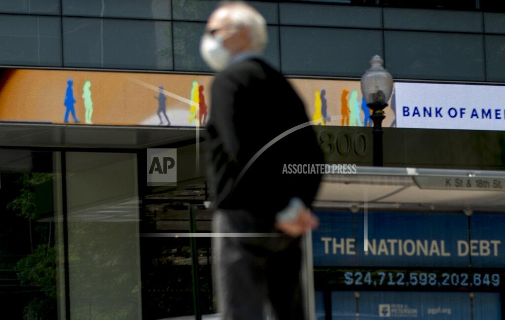 Andrew Harnik FILE - In this April 29, 2020 file photo, a man wearing a mask to protect against coronavirus, waits to cross the street as a digital sign displays groups of people walking above another sign displaying the size of the national debt along an empty K Street in Washington. The Congressional Budget Office has warned that the government this year will run the largest budget deficit, as a share of the economy, since 1945, the year World War II ended. Next year, the federal debt — made up of the year-after-year gush of annual deficits — is forecast to exceed the size of the entire American economy for the first time since 1946. (AP Photo/Andrew Harnik, File)