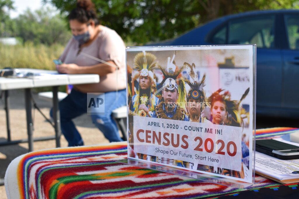 A sign promoting Native American participation in the U.S. census is displayed as Selena Rides Horse enters information into her phone on behalf of a member of the Crow Indian Tribe in Lodge Grass, Mont. on Wednesday, Aug. 26, 2020. There are more than 300 Native American reservations across the country, and almost all lag the rest of the country in participation in the census. (AP Photo/Matthew Brown)