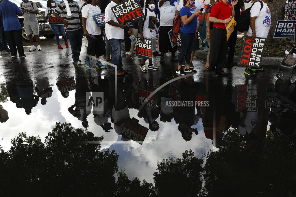 Rebecca Blackwell People carrying signs supporting voting rights are reflected in a puddle as they arrive at an early voting center at Model City Branch Library, as part of a "Souls to the Polls" march, in Miami, Sunday, Nov. 1, 2020. As Election Day closes in, Americans are exhausted from constant crises, on edge because of volatile political divisions and anxious about what will happen next.(AP Photo/Rebecca Blackwell)
