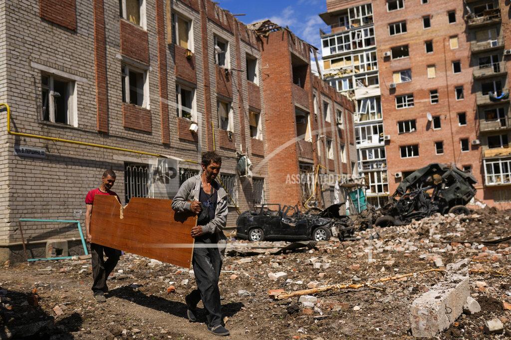 Francisco Seco Two men carry a wooded panel next to heavily damaged buildings and destroyed cars in a Russian bombing in Bakhmut, eastern Ukraine, Tuesday, May 24, 2022. The town of Bakhmut has been coming under increasing artillery strikes, particularly over the last week, as Russian forces try to press forward to encircle the city of Sieverodonetsk to the northeast. (AP Photo/Francisco Seco)