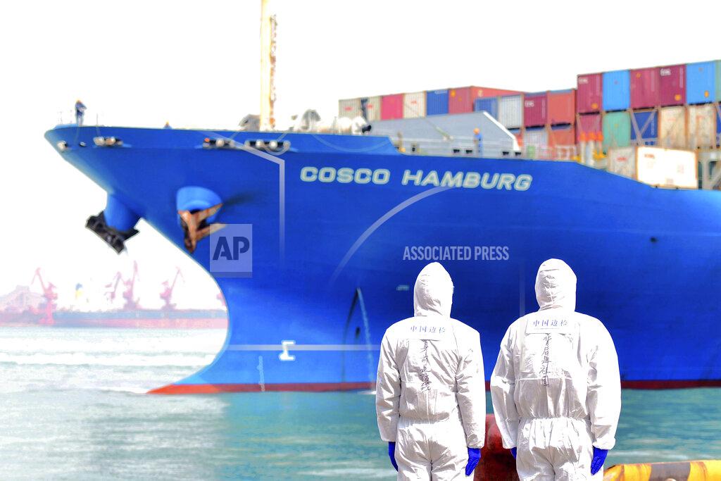 Uncredited FILE - In this March 31, 2020 file photo, workers in protective suits stand near a COSCO container ship docked at a port in Qingdao in eastern China's Shandong Province. China won’t restrict exports of medical goods needed to fight the coronavirus pandemic, a government spokesman said Thursday, April 16, amid global tension over scarce masks and ventilators. (Chinatopix via AP, File)