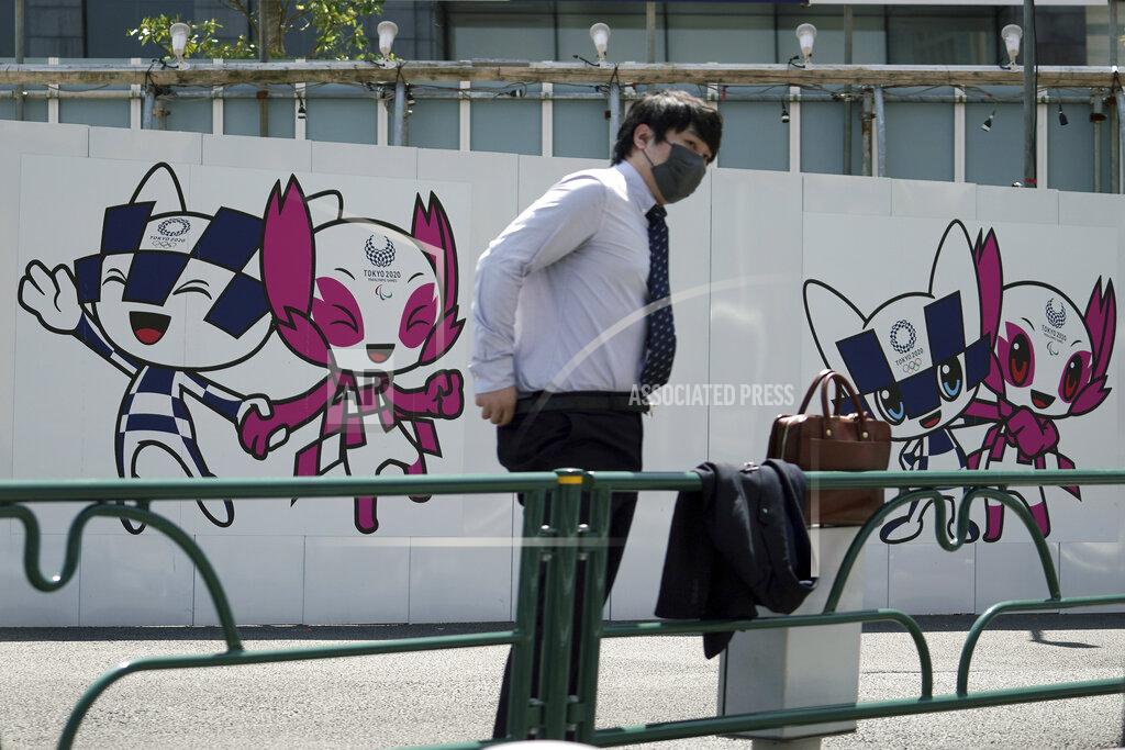 Eugene Hoshiko A man wearing a protective mask to help curb the spread of the coronavirus stands near drawings of Miraitowa and Someity, official mascots for the Tokyo 2020 Olympics and Paralympics, on a construction wall Tuesday, April 20, 2021, in Tokyo. (AP Photo/Eugene Hoshiko)