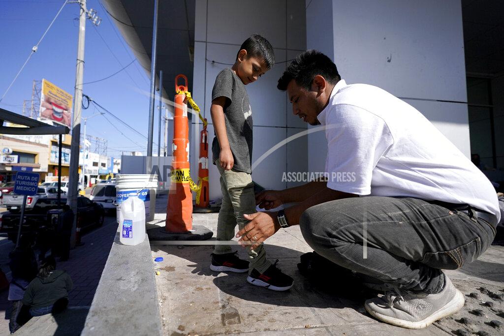 Julio Cortez Franklin Reyes, right, a migrant from Honduras, uses a dampened T-shirt to clean the pants of his 7-year-old son, Joshuan Reyes, after they were deported by the U.S. Customs and Border Protection, Thursday, March 18, 2021, in Reynosa, Mexico. The father and son have spent two nights in a plaza near the Mexico customs office off the McAllen-Hidalgo International Bridge while trying to figure out their next move. A surge of migrants on the Southwest border has the Biden administration on the defensive. The head of Homeland Security acknowledged the severity of the problem Tuesday but insisted it's under control and said he won't revive a Trump-era practice of immediately expelling teens and children. (AP Photo/Julio Cortez)
