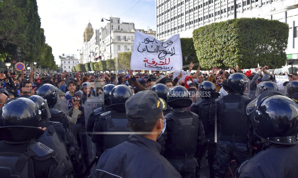 Hedi Ayari A demonstrator holds a poster reading " You push for illegal migration in a wooden boat," during a demonstration in Tunis, Saturday, Jan.23, 2021. Tunisia is extending its virus curfew and banning demonstrations as it tries to stem a rapid rise in infections and calm tensions after a week of protests and rioting over economic troubles. New clashes between protesters and police broke out Saturday hours after the new virus restrictions were announced. (AP Photo/Hedi Ayari)