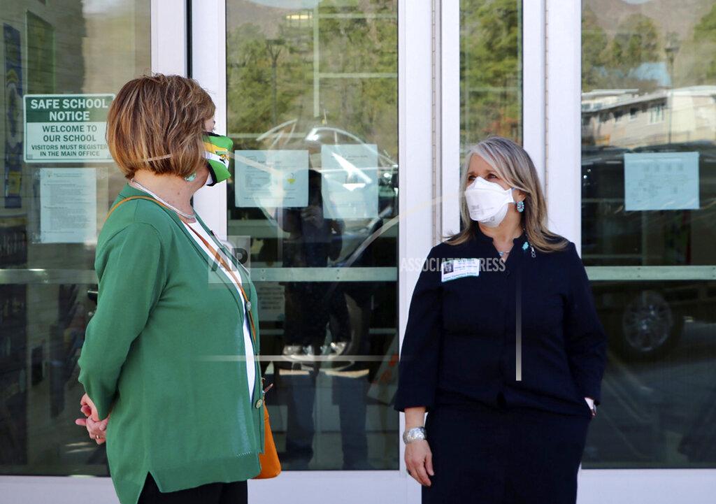 This photo provided by the Office of the Governor shows New Mexico Governor Michelle Lujan Grisham, right, is greeted by Aspen Elementary School Principal Michele Altherr, during a visit to Aspen Elementary School in Los Alamos on Monday, April 5, 2021. New Mexico's public schools are reopening for full-time, in-person learning this week. The shift to in-person learning is expected to relieve parent's year-long struggles with child care, unmet special needs, and spotty home internet. (Nora Meyers Sackett/Office of the Governor via AP)
