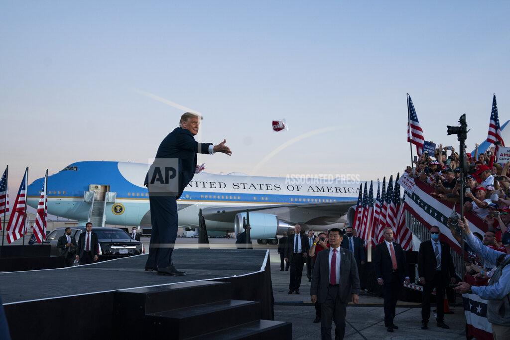 Evan Vucci President Donald Trump tosses face masks into the crowd as he arrives for a campaign rally at Orlando Sanford International Airport, Monday, Oct. 12, 2020, in Sanford, Fla. (AP Photo/Evan Vucci)