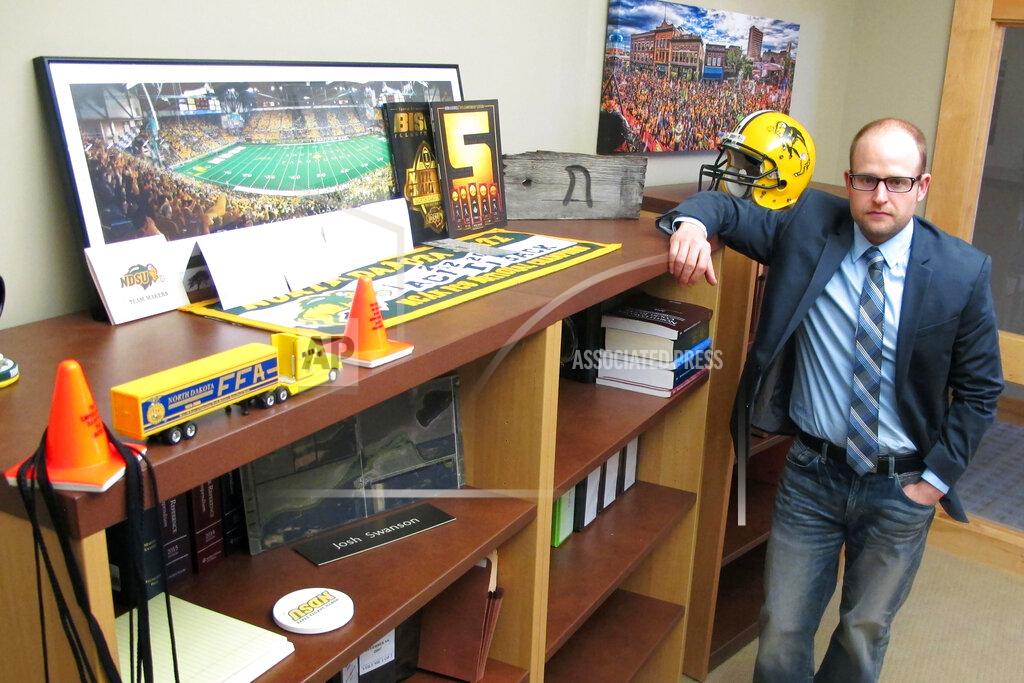 FILE - In this March 18, 2016, file photo, Fargo attorney Josh Swanson, of the Vogel Law Firm in Fargo, N.D., poses in his office next to a bookcase that contains numerous items of memorabilia from his alma mater North Dakota State University. NDSU seems to have perfected the art of reloading. The Bison are 12-0 and the top seed again in the FCS playoffs despite breaking in a new coach and a new quarterback this season. But with all their winning, seven of the last eight championships, is it all starting to get a little routine in Fargo? (AP Photo/Dave Kolpack, File)