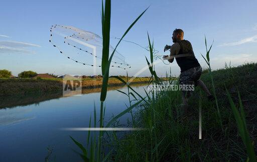 A man casts a net into a canal, Tuesday, Sept. 14, 2021, in McAllen, Texas. Canals used to deliver water in many parts of the Rio Grande Valley lose anywhere from 10% to 40% of the water they carry to seepage and evaporation, according to the Texas Water Development Board, making water a growing concern amid climate change and rising demand that scientists predict will lead to water shortages in the region by 2060.(AP Photo/Eric Gay)