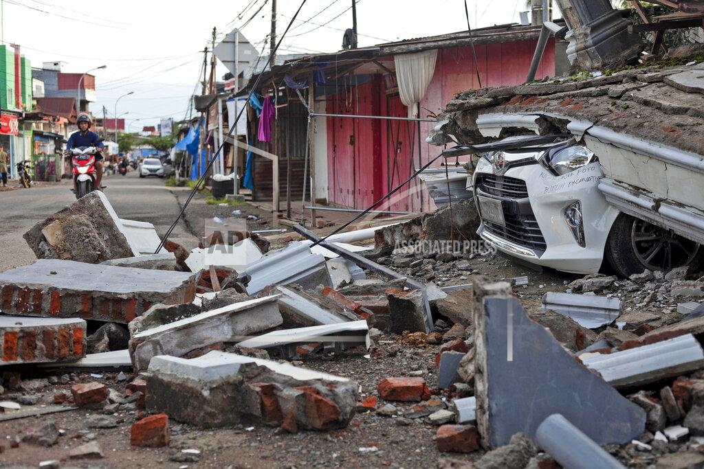 Yusuf Wahil A motorist rides past the wreckage of a car buried under the rubble of a building collapsed in Friday's earthquake in Mamuju, West Sulawesi, Indonesia, Monday, Jan. 18, 2021. Aid was reaching the thousands of people left homeless and struggling after an earthquake that killed a number of people in the province where rescuers intensified their work Monday to find those buried in the rubble. (AP Photo/Yusuf Wahil)