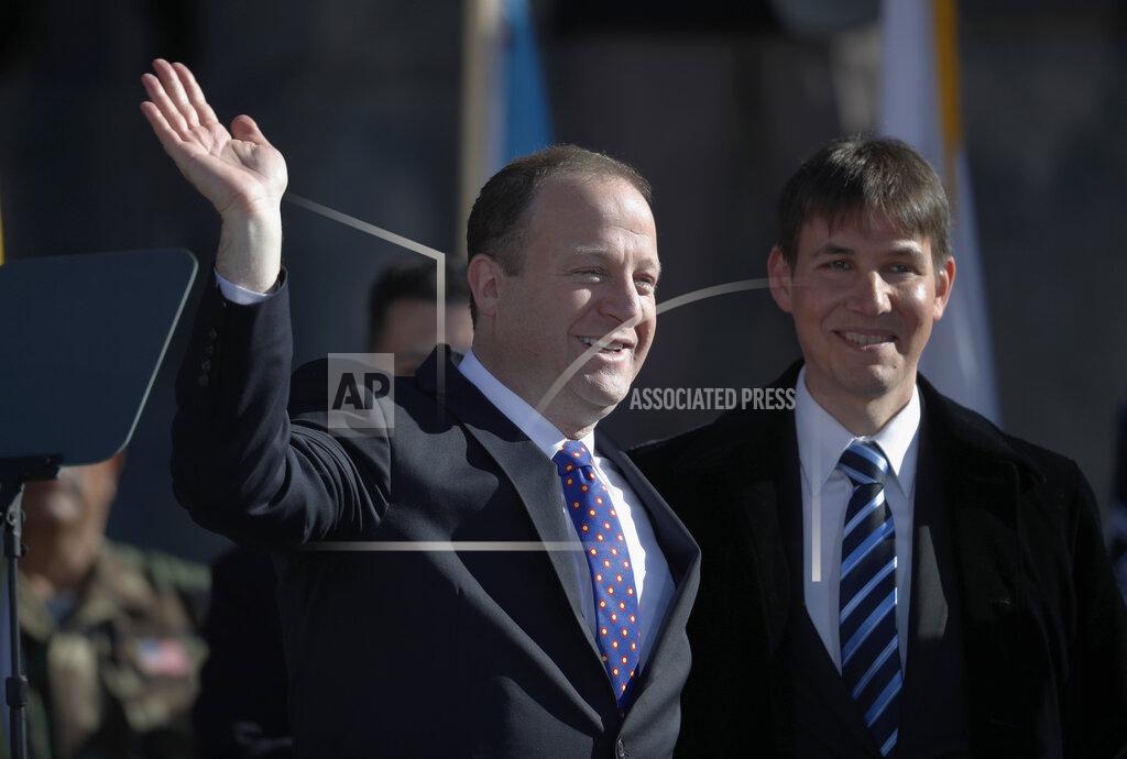 David Zalubowski FILE - In this Tuesday, Jan. 8, 2019 file photo, Colorado Gov. Jared Polis, left, joins his partner, Marlon Reis, in acknowledging the crowd after Polis took the oath of office during the inauguration ceremony in Denver. Colorado Gov. Jared Polis has tested positive for the coronavirus. Polis and his partner, Marlon Reis, both have COVID-19 and are asymptomatic, the governor said in a statement Saturday night, Nov. 28, 2020. (AP Photo/David Zalubowski, Pool)