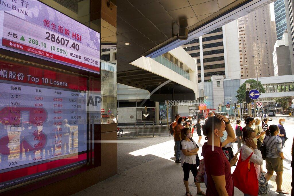 People walk past a bank's electronic board showing the Hong Kong share index in Hong Kong Tuesday, March 30, 2021. Asian shares were mixed in listless trading Tuesday after U.S. stocks finished mostly lower as cause for optimism, such as the Suez Canal reopening, mixed with caution about the vaccine rollout. (AP Photo/Vincent Yu)