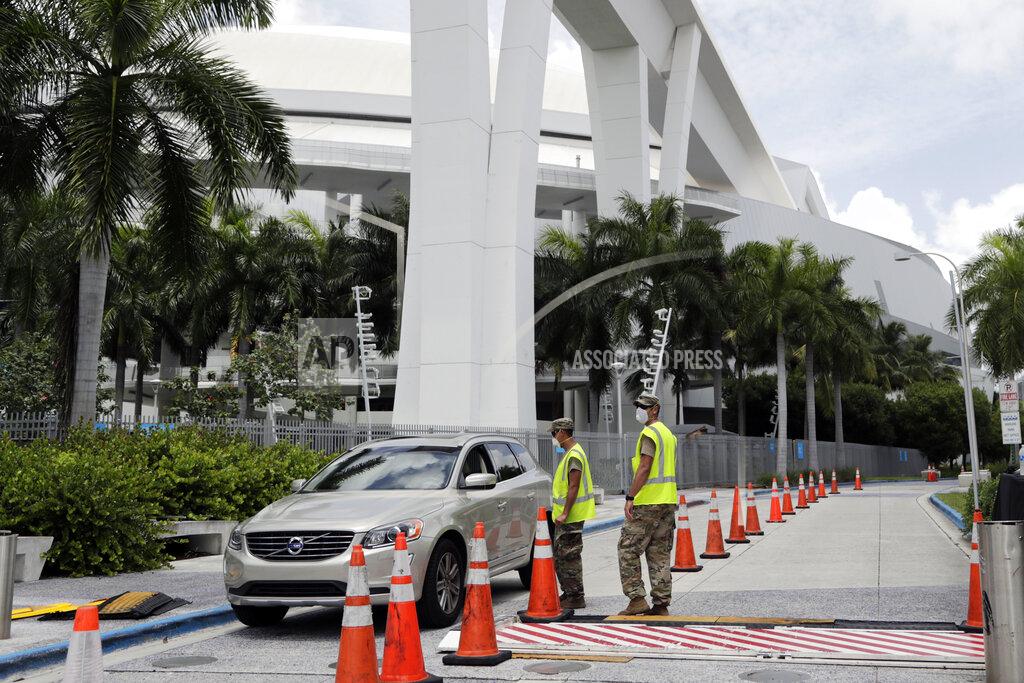 Lynne Sladky Members of the Florida National Guard monitor vehicles at a COVID-19 testing site outside of Marlins Park, Monday, July 27, 2020, in Miami. The Marlins home opener against the Baltimore Orioles on Monday night has been postponed as the Marlins deal with a coronavirus outbreak that stranded them in Philadelphia. (AP Photo/Lynne Sladky)