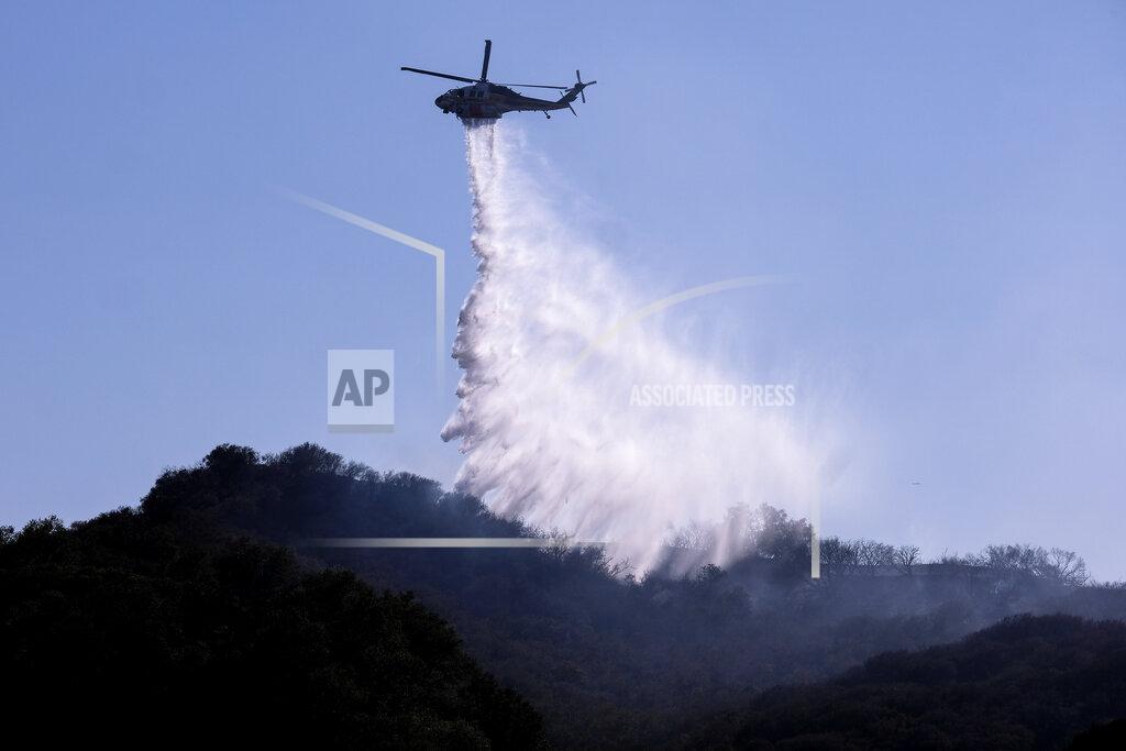 Ringo H.W. Chiu A A helicopter makes a water drop to put out hotspots in a wildfire in Topanga, west of Los Angeles, Monday, July 19, 2021. A brush fire scorched about 15 acres in Topanga today, initially threatening some structures before fire crews got the upper hand on the blaze, but one firefighter suffered an unspecified minor injury. (AP Photo/Ringo H.W. Chiu)