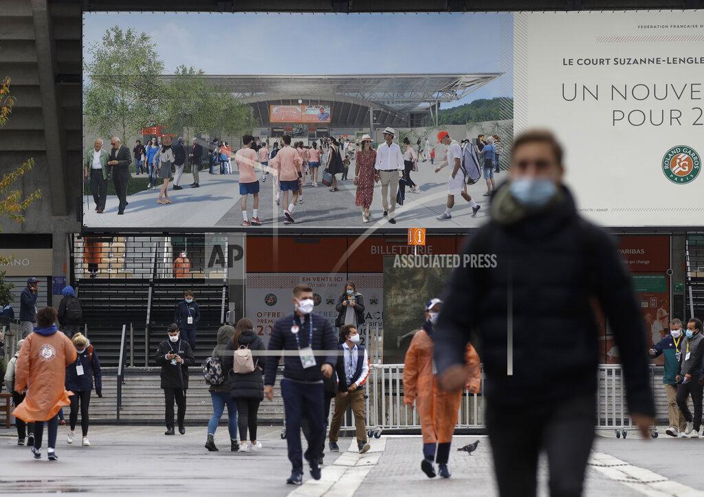 Alessandra Tarantino The image on a billboard of spectators with straw hats walking the sunny lanes of the Roland Garros grounds contrasts with the changed reality as spectators with face mask walk under damp and cold conditions during first round matches of the French Open tennis tournament at the Roland Garros stadium in Paris, France, Sunday, Sept. 27, 2020. (AP Photo/Alessandra Tarantino)