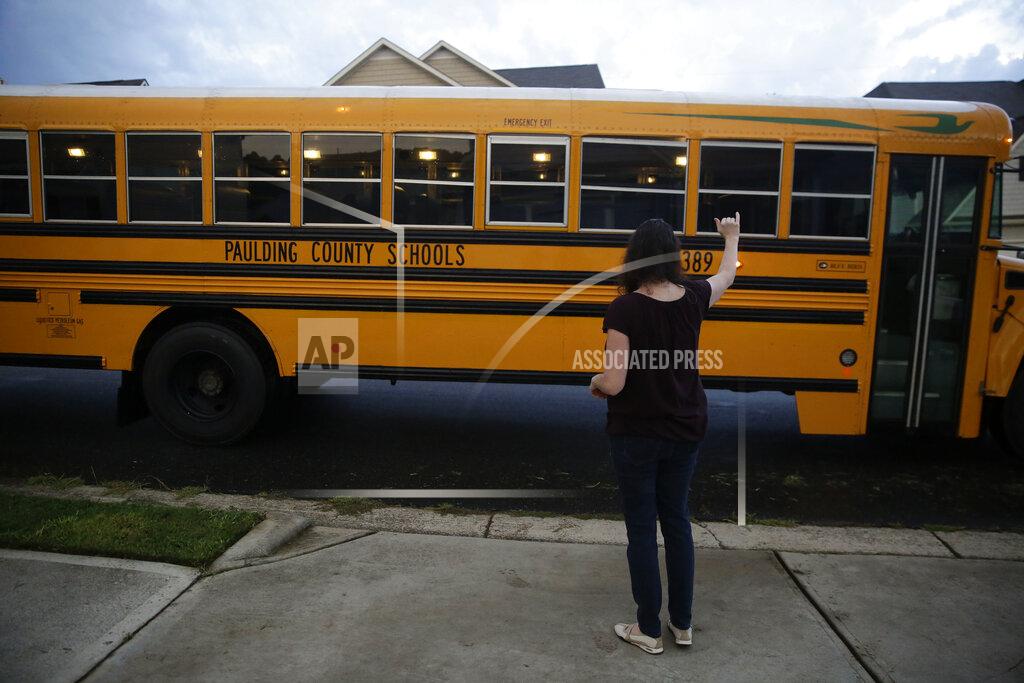 Brynn Anderson Rachel Adamus waves goodbye to her two children, Paul and Neva, as they ride the bus for the first day of school on Monday, Aug. 3, 2020, in Dallas, Ga. (AP Photo/Brynn Anderson)