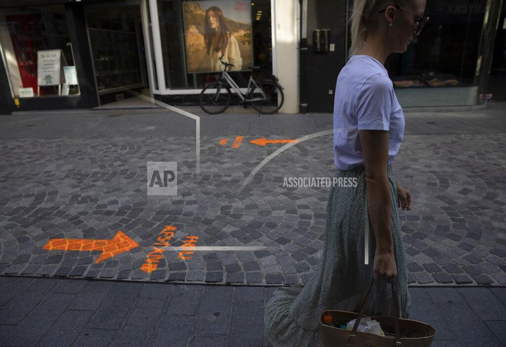 Virginia Mayo A woman follows physical distancing arrows as she walks on a shopping street, during a partial lifting of coronavirus, COVID-19, regulations in Halle, Belgium, Wednesday, June 24, 2020. (AP Photo/Virginia Mayo)