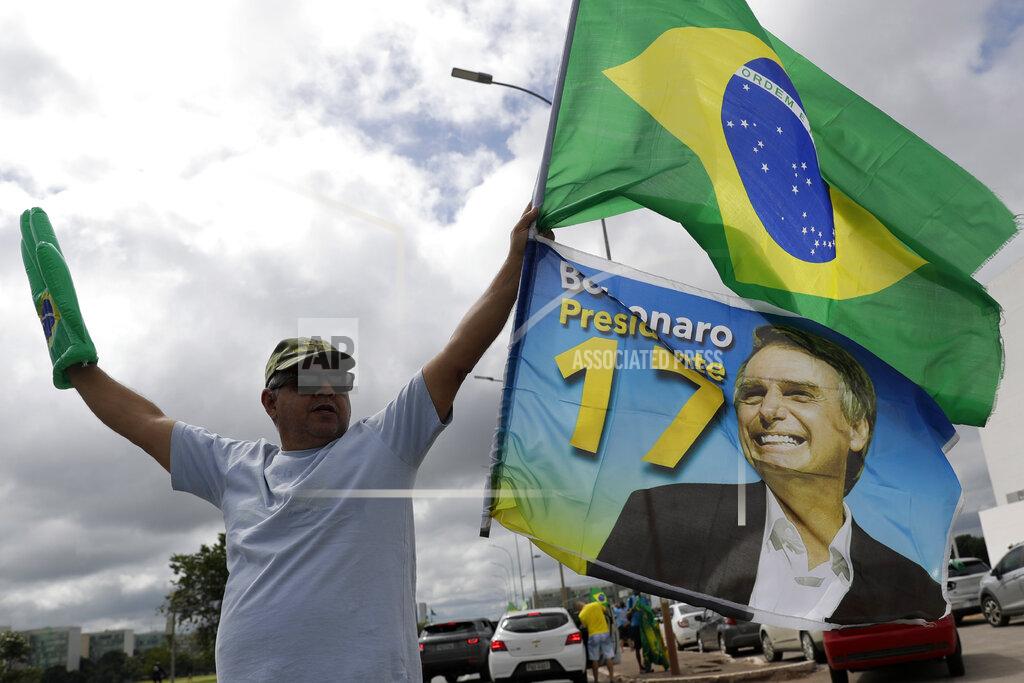 A demonstrator carries a Brazilian flag and a flag with an image of Brazil's President Jair Bolsonaro during a caravan celebrating Bolsonaro's 66th birthday, in Brasilia, Brazil, Sunday, March 21, 2021. (AP Photo/Eraldo Peres)