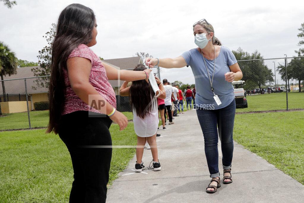 Lynne Sladky In this Sunday, June 7, 2020, photo, Gretel Cacerces, right, passes out masks to those standing in line for COVID-19 testing at the Florida Department of Health in Collier County amid the new coronavirus pandemic in Immokalee, Fla. Even as the pace of new cases has moderated in the state of Florida, this poor farmworking town in rural Florida is in the throes of an outbreak. (AP Photo/Lynne Sladky)