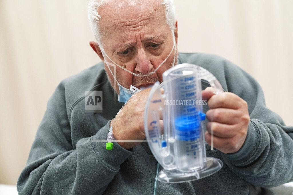 David Goldman COVID-19 patient Nicholas DiPompo, 78, uses an incentive spirometer to build up his lung capacity while recovering at a field hospital operated by Care New England set up in a former bank call center to handle a surge of COVID-19 patients in Cranston, R.I, Monday, Dec. 28, 2020. DiPompo spent three weeks at the field hospital recovering before being strong enough to go home. (AP Photo/David Goldman)