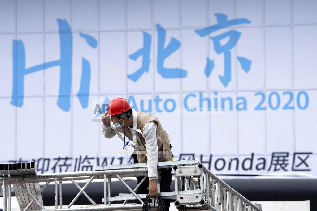Ng Han Guan A worker labors on Thursday, Sept. 24, 2020, near a sign which reads "Hi Beijing, Auto China 2020" ahead of the Auto China 2020 show to be held in Beijing. Auto executives are flying in early to wait out a coronavirus quarantine ahead of the Beijing auto show, the year's biggest sales event for a global industry that is struggling with tumbling sales and layoffs. (AP Photo/Ng Han Guan)