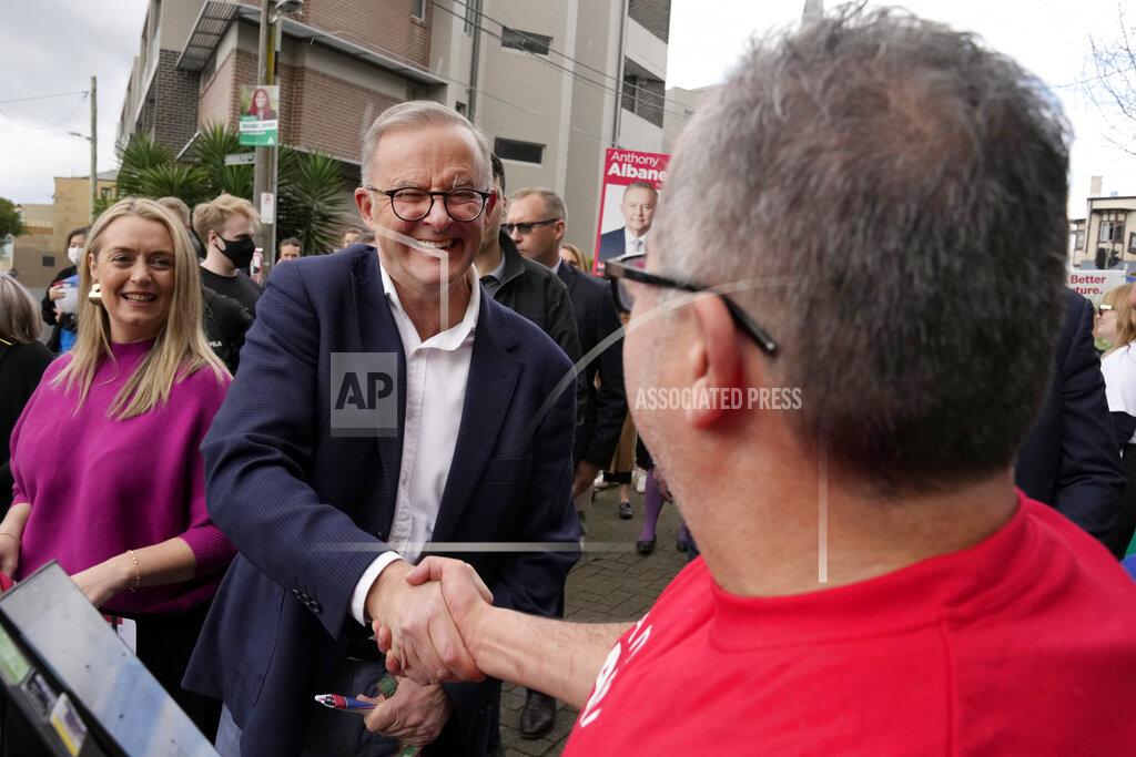 Rick Rycroft Labor Party leader Anthony Albanese, center, shakes hands with a voter he and his partner Jodie Haydon, left, arrive a polling place to cast their ballots in Sydney, Australia, Saturday, May 21, 2022. Australians go to the polls following a six-week election campaign that has focused on pandemic-fueled inflation, climate change and fears of a Chinese military outpost being established less than 1,200 miles off Australia's shore. (AP Photo/Rick Rycroft)