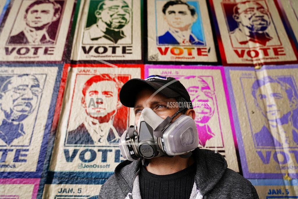 Brynn Anderson Artist Brandon Litman looks on as posters of U.S. Senator-elect's Jon Ossoff, D-Ga., and Raphael Warnock tower behind him after Georgia's Senate runoff race on Sunday, Jan. 10, 2021, in Atlanta. (AP Photo/Brynn Anderson)