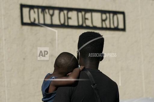 A Haitian migrant carries a boy while waiting to board a bus provided by a humanitarian group after being released from U.S. Customs and Border Protection custody, Friday, Sept. 24, 2021, in Del Rio, Texas. The “amistad,” or friendship, that Del Rio, Texas, and Ciudad Acuña, Mexico, celebrate with a festival each year has been important in helping them deal with the challenges from a migrant camp that shut down the border bridge between the two communities for more than a week. Federal officials announced the border crossing would reopen to passenger traffic late Saturday afternoon and to cargo traffic on Monday. (AP Photo/Julio Cortez)