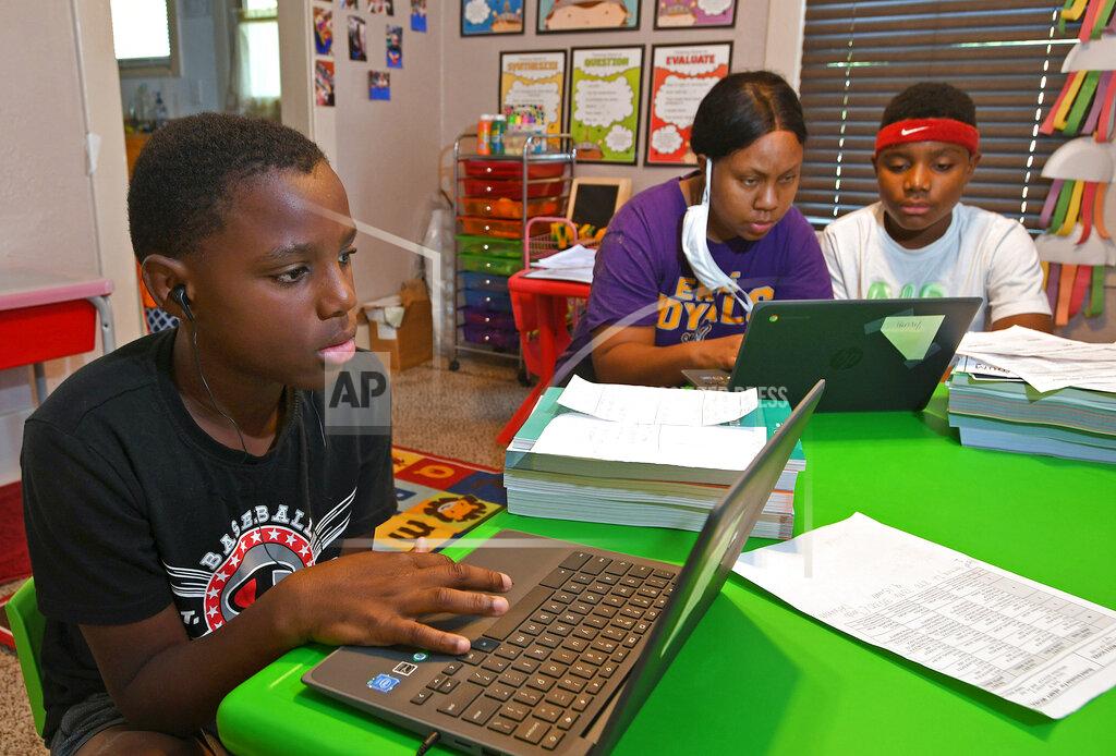 Christopher Millette FILE—In this file photo from Sept. 8, 2020, Michael Henry, 11, left, sits with his mother Mary Euell, center, and his brother Mario Henry, 12, as they work through math lessons remotely at their west Erie, Pa. on the first day of classes for the Erie School District. Most of the district's 11,000 students began the school year with remote learning due to COVID-19. Gov. Tom Wolf will ask lawmakers Wednesday, Feb. 3, 2021, to raise income taxes on higher earners and give public schools a massive boost in aid, even as he faces a gaping deficit and uncertainty over how much more pandemic relief the federal government will send. (Christopher Millette/Erie Times-News via AP, File)