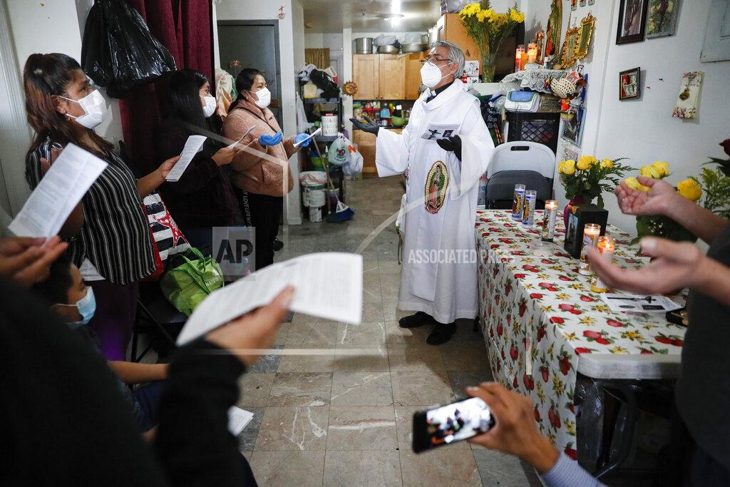 John Minchillo Fabian Arias, a Lutheran pastor with Saint Peter's Church in Manhattan, right, gives an in-home funeral service surrounded by family members of Graciela Ruiz Martinez who died of COVID-19, Sunday, May 10, 2020, in the Queens borough of New York. (AP Photo/John Minchillo)
