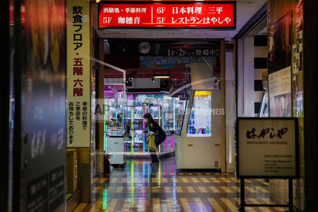 Kiichiro Sato A couple play an arcade machine as people walk around and gather at a bar after government imposed 8 p.m. closing time for restaurants and bars under Tokyo's fourth state of emergency Saturday, July 17, 2021, in Tokyo. The latest state of emergency has asked restaurants and bars to close by 8 p.m., if not entirely. This has pushed people to drink outside, although many bars remain open and bustling with customers who are defying the rules and expressing frustration and indifference. (AP Photo/Kiichiro Sato)