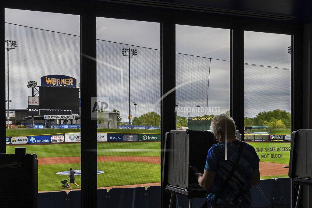 Chris Machian Head Groundskeeper Zach Ricketts, left, works on the field while Carol Szczepaniak, right, votes in Nebraska's primary election at Werner Park, which is home to the AAA baseball team, the Omaha Storm Chasers on Tuesday, May 10, 2022, in Papillion, Neb. (Chris Machian/Omaha World-Herald via AP)