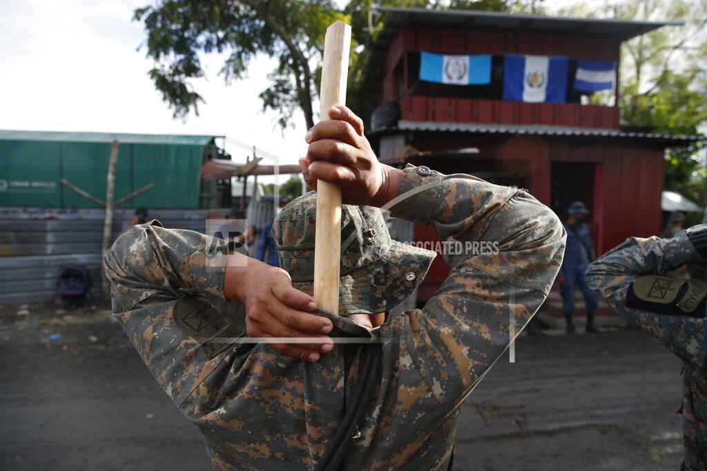 Moises Castillo A soldier places a hand made, wooden stick into the back of his uniform as he stands guard in El Cinchado, Guatemala, on the border with Honduras, Friday, Oct. 2, 2020. Guatemala vowed to detain and return members of a new caravan of about 2,000 migrants that set out from neighboring Honduras in hopes of reaching the United States, saying they represent a health threat amid the coronavirus pandemic. (AP Photo/Moises Castillo)