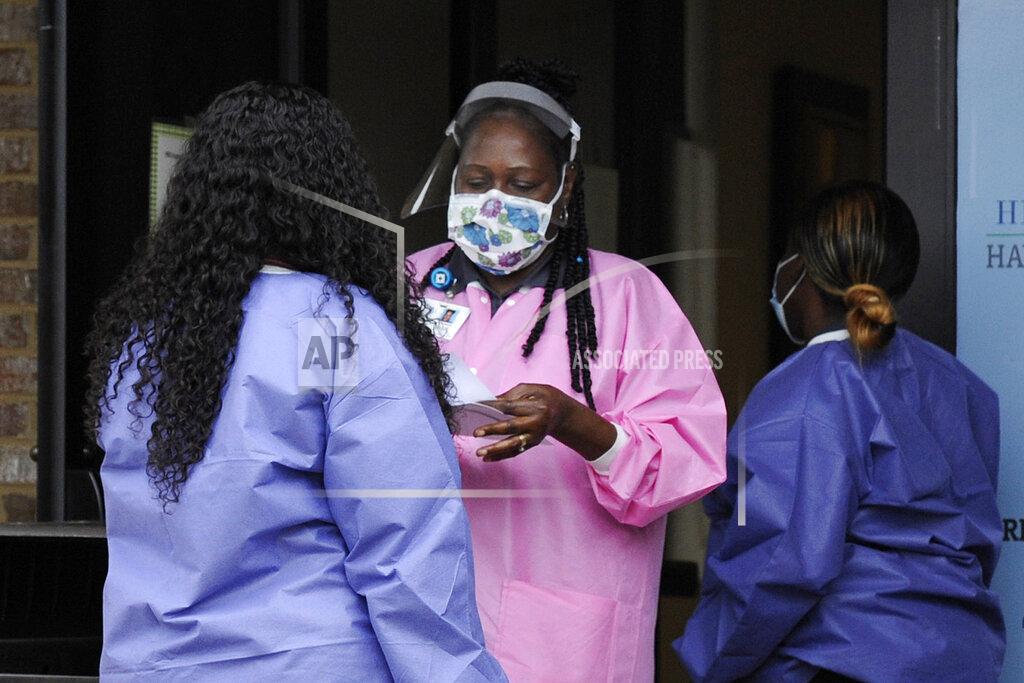 Jay Reeves FILE - In this May 27, 2020, file photo, health care workers talk outside a Lowndes County coronavirus testing site in Hayneville, Ala. Experts say Lowndes County and nearby poor, mostly black counties in rural Alabama are now facing a "perfect storm" as infections tick up: a lack of access to medical care combined with poverty and the attendant health problems that can worsen the outcomes for those who become sick. (AP Photo/Jay Reeves, File)