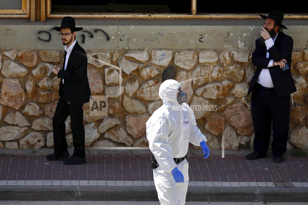 Ariel Schalit An Israeli police officer wears protective gear as two ultra-Orthodox men detained by police wait outside a synagogue on a mainly deserted street because of the government's measures to help stop the spread of the coronavirus, in Bnei Brak, a suburb of Tel Aviv, Israel, Thursday, April 2, 2020. On Wednesday, Israeli Prime Minister Benjamin Netanyahu ordered a police cordon around the largely ultra-Orthodox city of Bnei Brak, to limit movement to and from the city. Bnei Brak has the second highest number of coronavirus cases in Israel. (AP Photo/Ariel Schalit)