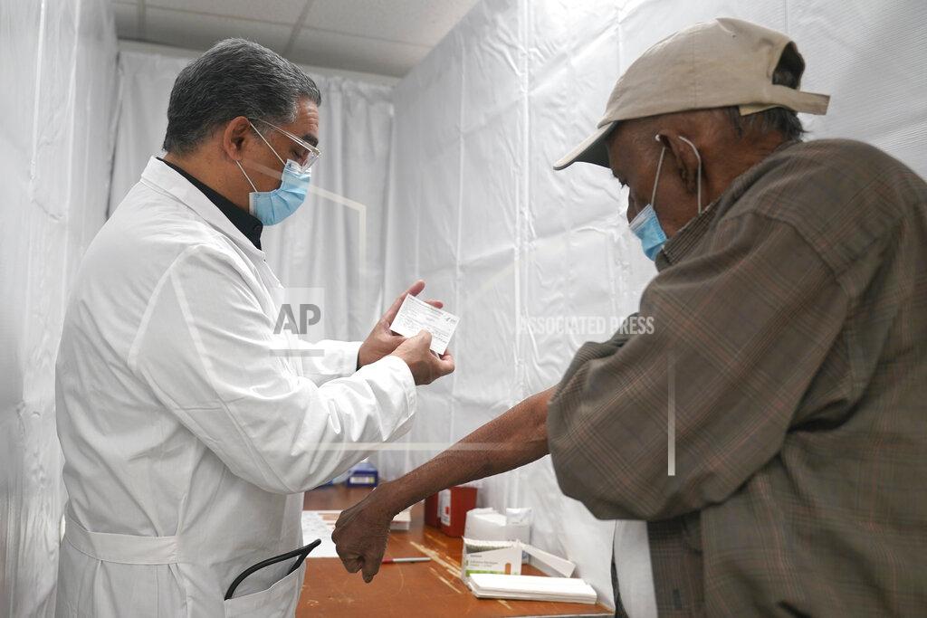 Seth Wenig Dr. Victor Peralta, left, examines Sundar Surujmohan vaccination card before giving him his second dose of the COVID-19 vaccine in New York, Friday, Feb. 5, 2021. From elderly Cuban Americans in Florida to farmworkers in California, Latinos face daunting barriers like fear, language and a lack of education and access as the COVID-19 vaccines roll out, creating risks for public health as the virus mutates and spreads. (AP Photo/Seth Wenig)