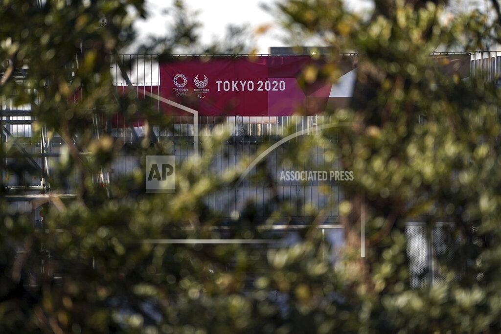 Eugene Hoshiko A banner of Tokyo 2020 Olympic and Paralympic games is seen though tree branches of Canoe Slalom Course, one of the venues of Tokyo 2020 Olympic and Paralympic games, in Tokyo Thursday, Jan. 21, 2021. The postponed Tokyo Olympics are to open in just six months. Local organizers and the International Olympic Committee say they will go ahead on July 23. But it’s still unclear how this will happen with virus cases surging in Tokyo and elsewhere around the globe. (AP Photo/Eugene Hoshiko)