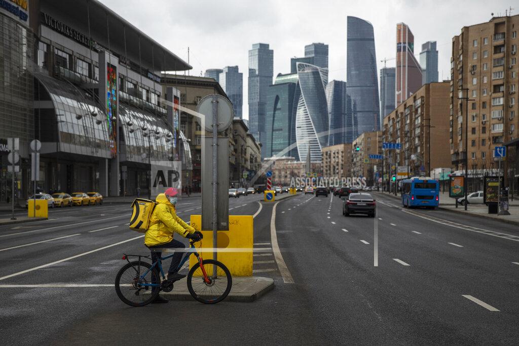 Pavel Golovkin A food delivery courier wearing a face mask waits to cross a nearly empty road due to residents taking the advice of staying at home to avoid the spread of the coronavirus, with Moscow City skyscrapers in the background, in Moscow, Russia, Thursday, April 2, 2020. Online shopping for food and other supplies has boomed in Moscow after the authorities put most residents on lockdown. The new coronavirus causes mild or moderate symptoms for most people, but for some, especially older adults and people with existing health problems, it can cause more severe illness or death. (AP Photo/Pavel Golovkin)