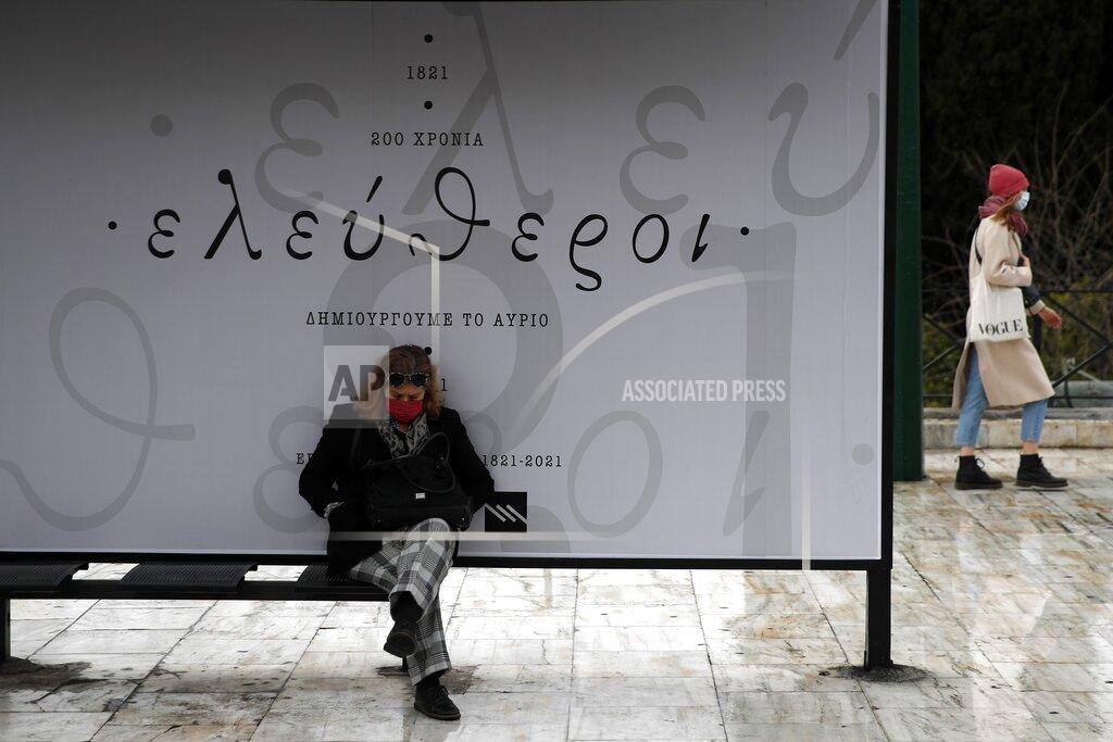 Thanassis Stavrakis A woman sits at a bus stop as the sign reads "1821, 200 years, free to create tomorrow" ahead of a military parade, in Athens, Tuesday, March 23, 2021. The military parade on March 25, marking 200-years since the war that resulted in Greece's independence from the Ottoman Empire and rebirth as a nation, will be held without spectators due to the coronavirus. (AP Photo/Thanassis Stavrakis)