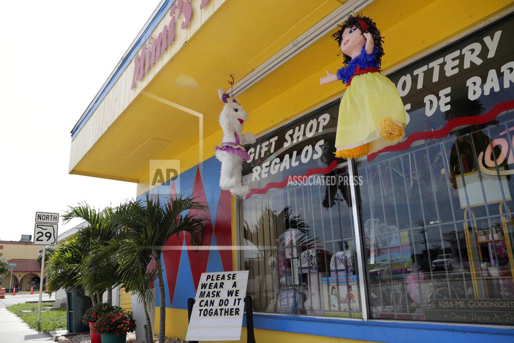 Lynne Sladky In this Monday, June 8, 2020, photo, a sign urging people to wear protective face masks is shown outside of Mimi's Piñata & Party Rentals shop amid the new coronavirus pandemic in Immokalee, Fla. Even as the pace of new cases has moderated in the state of Florida, this poor farmworking town in rural Florida is in the throes of an outbreak. (AP Photo/Lynne Sladky)