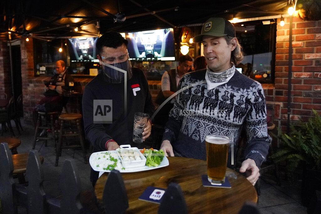 Marcio Jose Sanchez A waiter serves food to a customer at Ye Olde King's Head on Thursday, Nov. 19, 2020, in Santa Monica, Calif. The British restaurant and bar in seaside Southern California has been battered the past nine months and was in the process of adapting to new restrictions that took effect Friday, Nov. 20 that would further crimp its recovery even as the prospect of a crippling shutdown loomed. (AP Photo/Marcio Jose Sanchez)