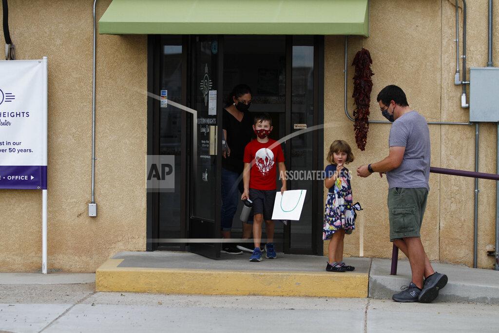 FILE - In this Aug. 10, 2020, file photo, public elementary school teachers Julia and Seth Hooper pick up their children Emry, 7, and Ivy, 4, at the Western Heights Learning Center in Albuquerque, N.M. More school districts in New Mexico can bring students back into classrooms in early February, Gov. Michelle Lujan Grisham announced Tuesday, Jan. 26, 2021. The Democratic governor said she's allowing schools to open their doors to students of all ages, in a major pull-back of restrictions that were based on county-level COVID-19 case rates and hospital capacity. (AP Photo/Cedar Attanasio, File)