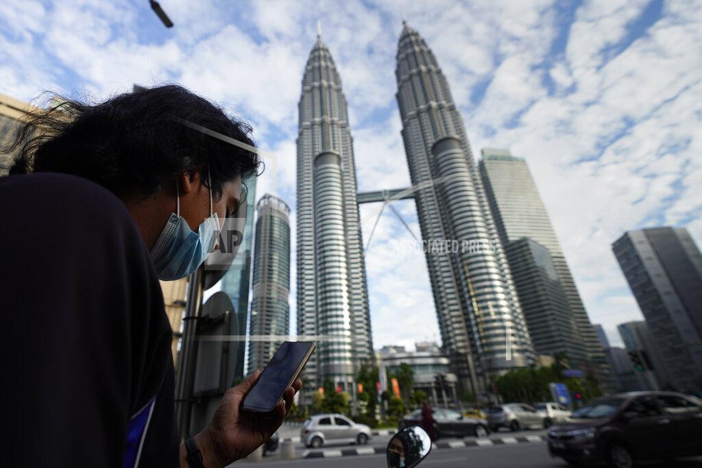 Vincent Thian A man wearing a face mask listens to live broadcast in front of Twin Towers in downtown Kuala Lumpur, Malaysia, Monday, Jan. 11, 2021. Prime Minister Muhyiddin Yassin says Malaysia’s health care system is at a breaking point as he announced new movement curbs, including near-lockdown in Kuala Lumpur and several high-risk states to rein in a spike in coronavirus cases. (AP Photo/Vincent Thian)