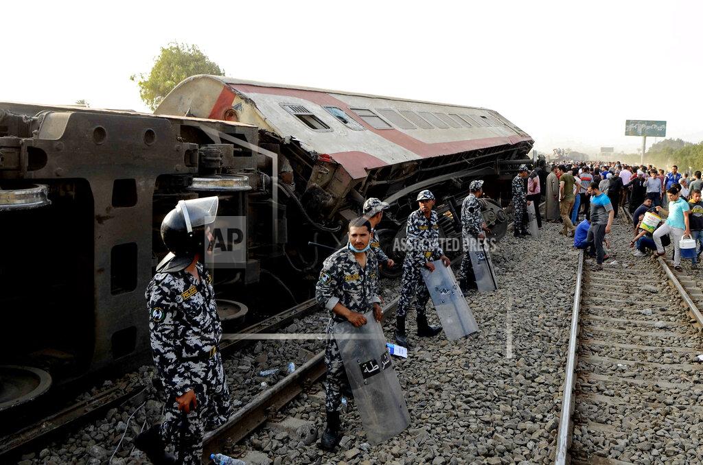Tarek Wagih Security forces stand guard as people gather at the site where a passenger train derailed injuring at least 100 people, near Banha, Qalyubia province, Egypt, Sunday, April 18, 2021. At least eight train wagons ran off the railway, the provincial governor's office said in a statement. (AP Photo/Tarek Wagih)